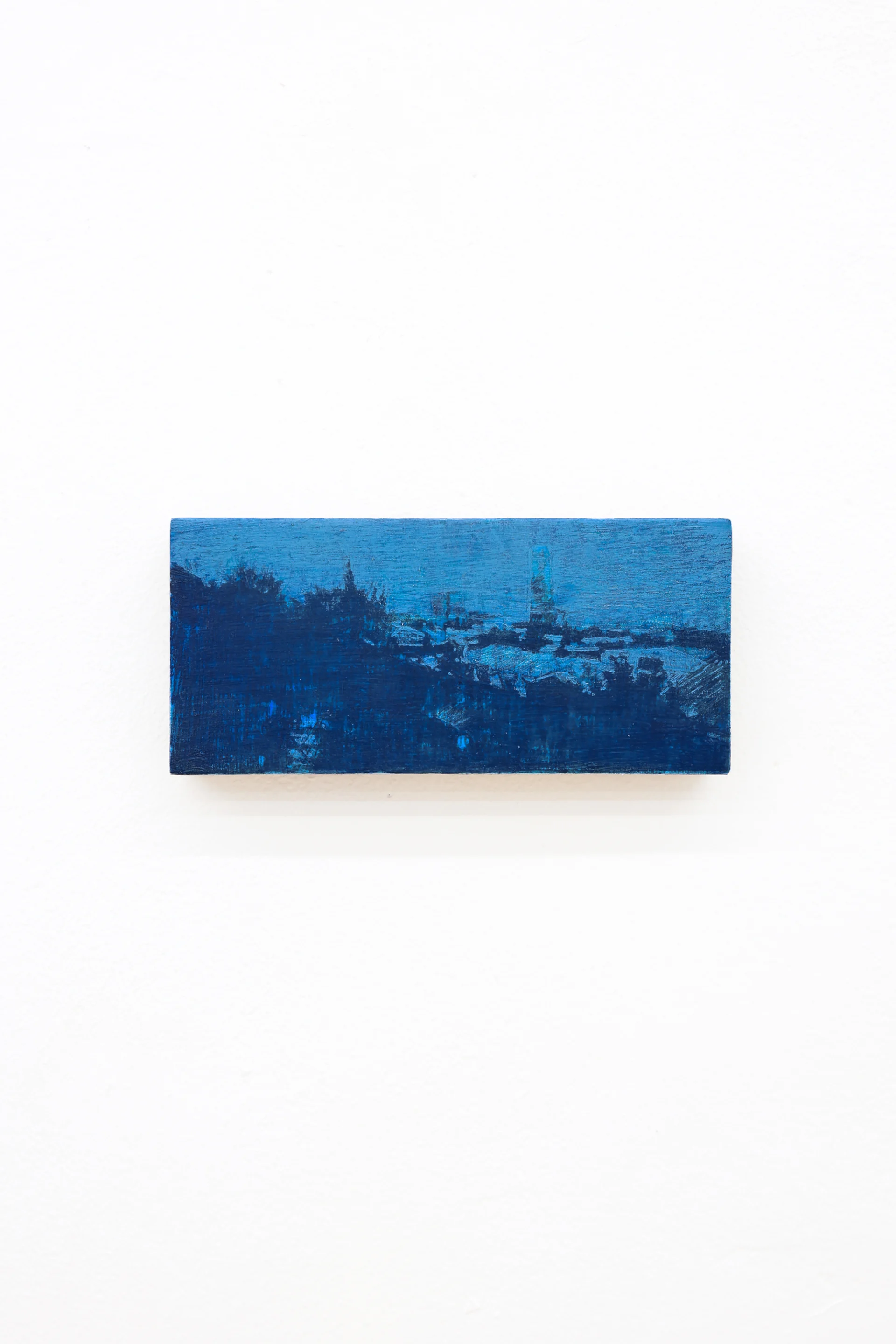Mtatsminda Turn 12. Deep cobalt and midnight-blue nocturne on an oak block, a hillside of buildings and a slender tower beneath a luminous blue sky.
